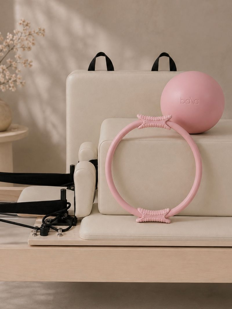 Pink Pilates ring and ball resting on a cream reformer in the private space