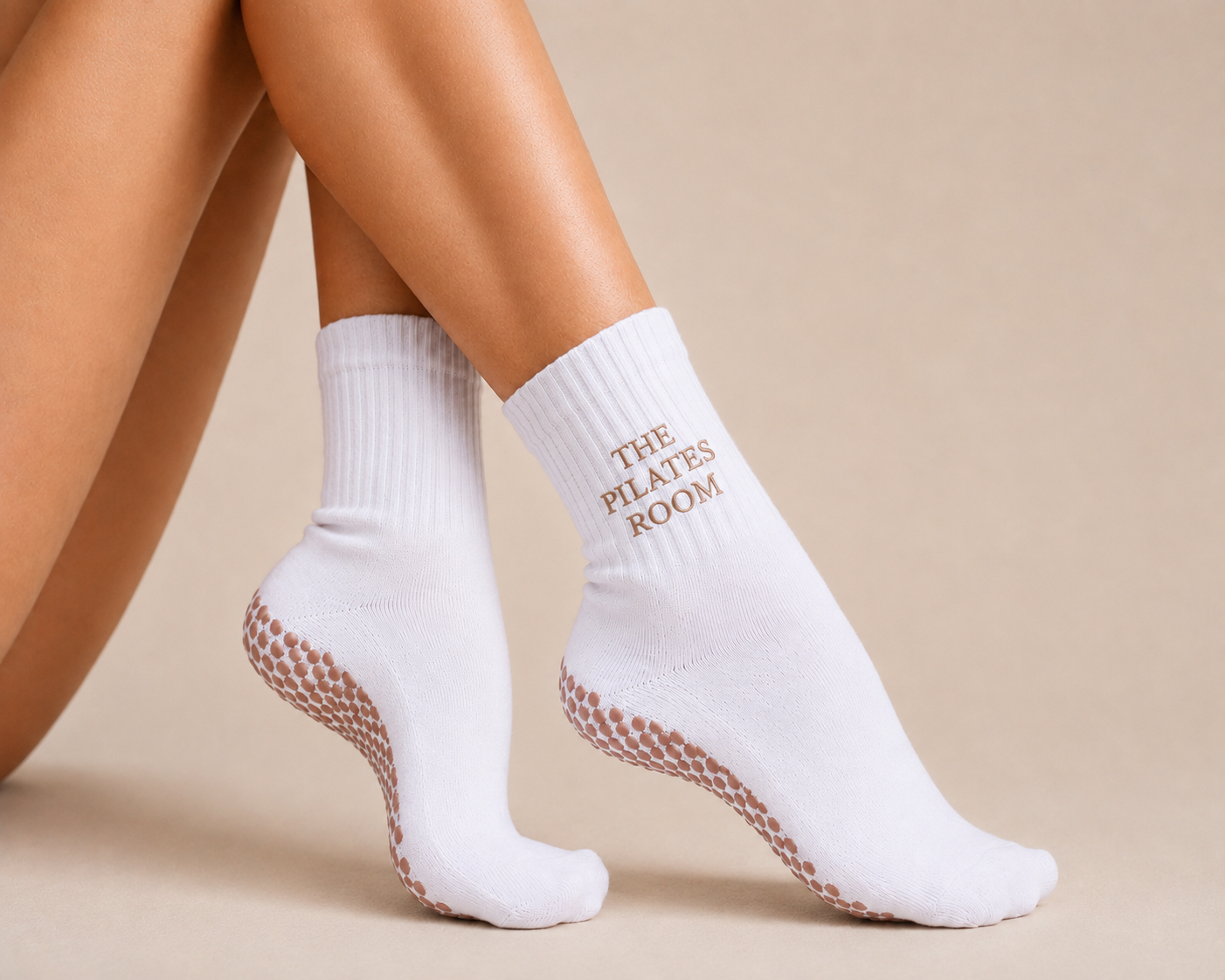 White ribbed The Pilates Room grip socks with tan grip dots, worn seated