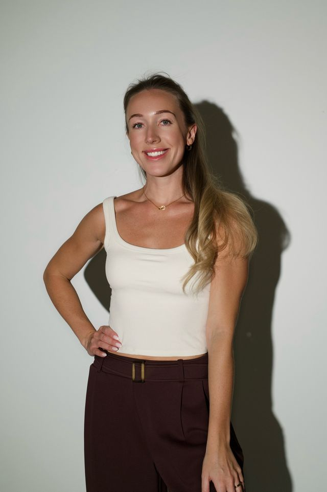 Chloe standing against a sunlit wall in a cream tank top and espresso trousers